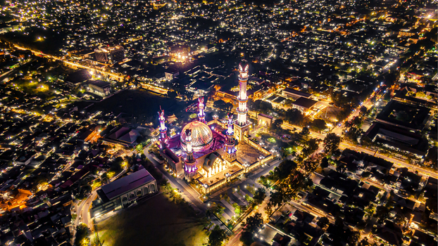 Aerial view of the illuminated Islamic Center NTB Hubbul Wathan Great Mosque at night surrounded by the glowing city lights of Kecamatan Selaparang Nusa Tenggara Barat Indonesia. Aerial view of the illuminated Islamic Center NTB Hubbul Wathan Great Mosque at night surrounded by the glowing city lights of Kecamatan Selaparang Nusa Tenggara Barat Indonesia.