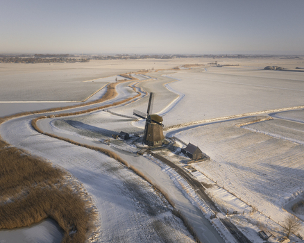 Aerial view of a traditional Dutch windmill standing beside a winding frozen canal in a snow covered landscape in Ursem North Holland Netherlands. Aerial view of a traditional Dutch windmill standing beside a winding frozen canal in a snow covered landscape in Ursem North Holland Netherlands.