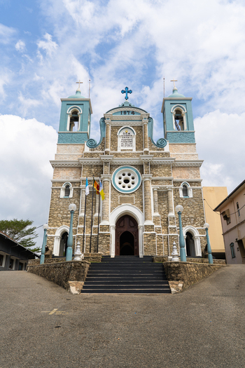 View of St. Mary s Cathedral featuring its historic stone facade and blue capped towers under a bright cloudy sky in Galle Southern Province Sri Lanka.