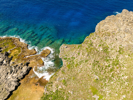 Aerial view of Chigit Beach with rugged limestone cliffs turquoise coastal waters and lush green vegetation in Northern Tinian Tinian Northern Mariana Islands. Aerial view of Chigit Beach with rugged limestone cliffs turquoise coastal waters and lush green vegetation in Northern Tinian Tinian Northern Mariana Islands.