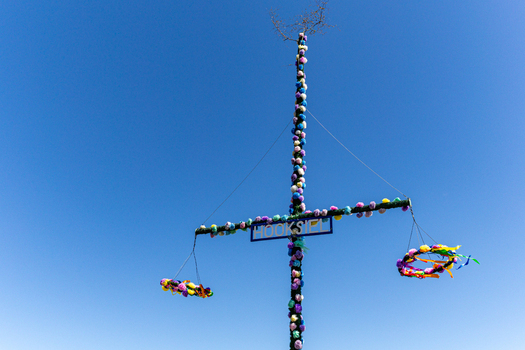 View of the decorated Hooksiel maypole adorned with colorful floral garlands and hanging wreaths under a clear blue sky in Wangerland Niedersachsen Germany. View of the decorated Hooksiel maypole adorned with colorful floral garlands and hanging wreaths under a clear blue sky in Wangerland Niedersachsen Germany.