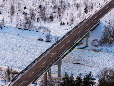Aerial view of a road bridge crossing a frozen river surrounded by snow covered banks and winter trees Lithuania. Aerial view of a road bridge crossing a frozen river surrounded by snow covered banks and winter trees Lithuania.