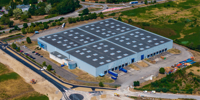 Aerial view of Hombourg Logistic park featuring a large warehouse with a flat roof skylights loading docks with parked trucks and parking areas in Hombourg Grand Est France.
