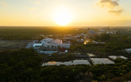 Aerial view of industrial warehouses and ponds surrounded by lush green vegetation during a golden sunset in Kecamatan Denpasar Selatan Bali Indonesia.