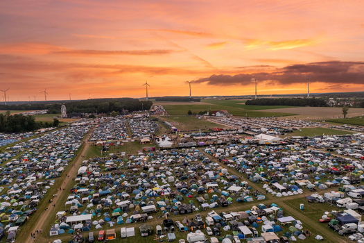 Aerial view of the Open Beatz Festival campsite with thousands of tents and cars under a vibrant sunset sky with wind turbines Herzogenaurach Bayern Germany. Aerial view of the Open Beatz Festival campsite with thousands of tents and cars under a vibrant sunset sky with wind turbines Herzogenaurach Bayern Germany.