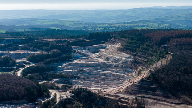 Aerial view of the stark white quarry contrasting with the surrounding dense green forest and distant rolling hills &Eacute;chassi&egrave;res Auvergne Rh&ocirc;ne Alpes France.
