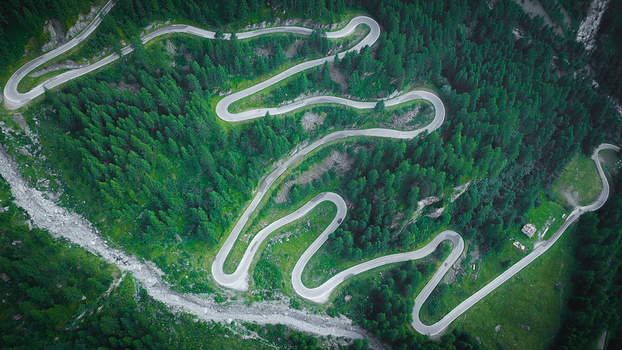 Aerial view of a winding mountain road with multiple hairpin turns through a dense coniferous forest in Heremence Valais Switzerland. Aerial view of a winding mountain road with multiple hairpin turns through a dense coniferous forest in Heremence Valais Switzerland.