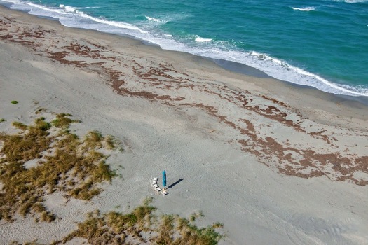 Aerial view of the shoreline where the golden sand meets the turquoise sea a lone paddleboard and chairs sit on the beach Jupiter Island Florida United States. Aerial view of the shoreline where the golden sand meets the turquoise sea a lone paddleboard and chairs sit on the beach Jupiter Island Florida United States.