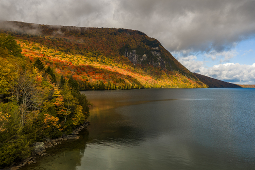 Aerial view of Lake Willoughby during peak autumn foliage with vibrant red and orange trees covering the mountainside calm water and cloudy sky in Westmore Vermont United States. Aerial view of Lake Willoughby during peak autumn foliage with vibrant red and orange trees covering the mountainside calm water and cloudy sky in Westmore Vermont United States.