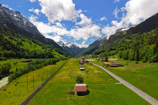 Aerial view of the lush green Grindelwald valley in the Swiss Alps with wooden huts a railway line and a road winding through the landscape in Grindelwald Canton of Bern Switzerland.