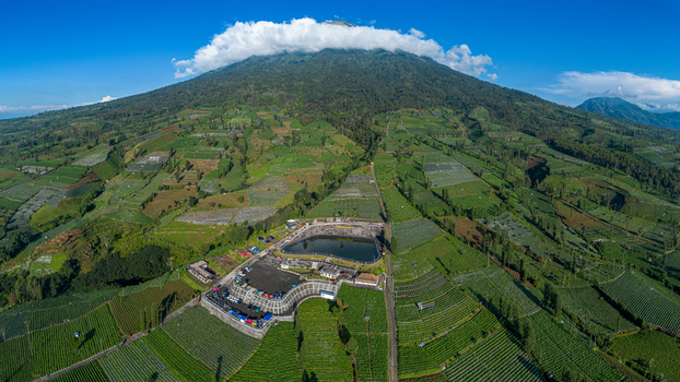 Aerial view of Embung Bansari reservoir on the slopes of Mount Sindoro surrounded by lush agricultural terraces and fields under a blue sky Temanggung Central Java Indonesia.