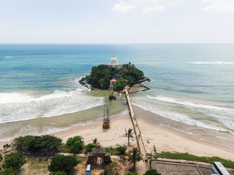 Aerial view of Parevi Duwa Temple on a small island connected by a bridge to the sandy beach with turquoise ocean waves in Matara Southern Province Sri Lanka. Aerial view of Parevi Duwa Temple on a small island connected by a bridge to the sandy beach with turquoise ocean waves in Matara Southern Province Sri Lanka.