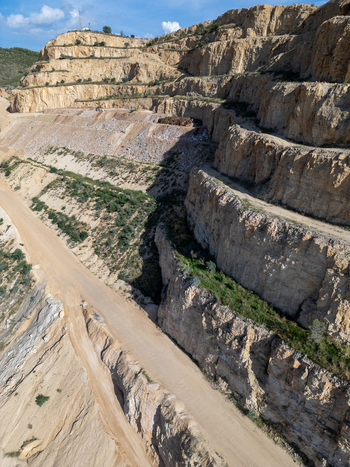 Aerial view of a large open pit stone quarry with terraced rock faces dirt access roads and excavation areas in Teulada Valencian Community Spain.