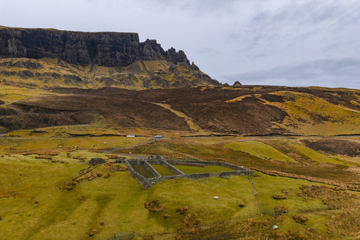Aerial view of The Quiraing landscape with a historic stone sheepfold on rolling green hills under an overcast sky Isle of Skye Scotland United Kingdom. Aerial view of The Quiraing landscape with a historic stone sheepfold on rolling green hills under an overcast sky Isle of Skye Scotland United Kingdom.