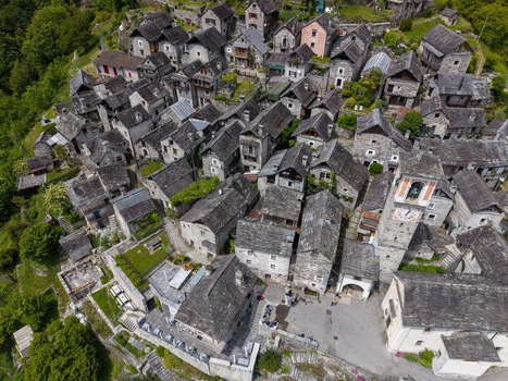 Aerial view of Corippo Albergo Diffuso and traditional stone houses with slate roofs nestled on a green hillside in Corippo Ticino Switzerland. Aerial view of Corippo Albergo Diffuso and traditional stone houses with slate roofs nestled on a green hillside in Corippo Ticino Switzerland.