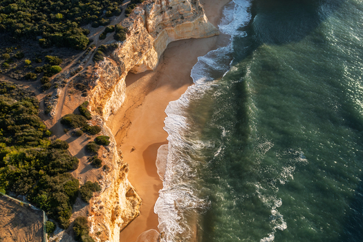 Aerial view of Caramujeira beach with golden sand dramatic limestone cliffs and turquoise ocean waves crashing on the shore in Lagoa Faro Portugal. Aerial view of Caramujeira beach with golden sand dramatic limestone cliffs and turquoise ocean waves crashing on the shore in Lagoa Faro Portugal.