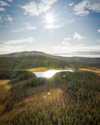 Aerial view of a serene lake nestled within a vast coniferous forest with rolling hills under a bright sun in Enontekio Lapland Finland. Aerial view of a serene lake nestled within a vast coniferous forest with rolling hills under a bright sun in Enontekio Lapland Finland.