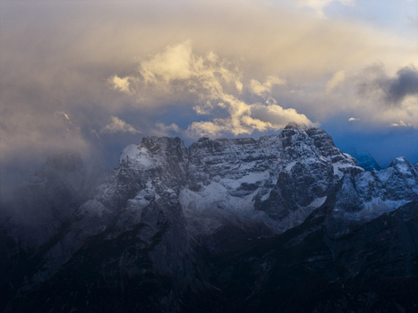 Aerial view of snow capped Tre Cime di Lavaredo peaks piercing through a veil of ethereal clouds their jagged edges softened by the golden light of the setting sun Misurina Veneto Italy. Aerial view of snow capped Tre Cime di Lavaredo peaks piercing through a veil of ethereal clouds their jagged edges softened by the golden light of the setting sun Misurina Veneto Italy.