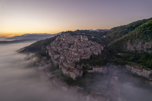 Aerial view of the historic town of Artena perched on a hillside above a sea of morning fog during sunrise in Artena Lazio Italy.