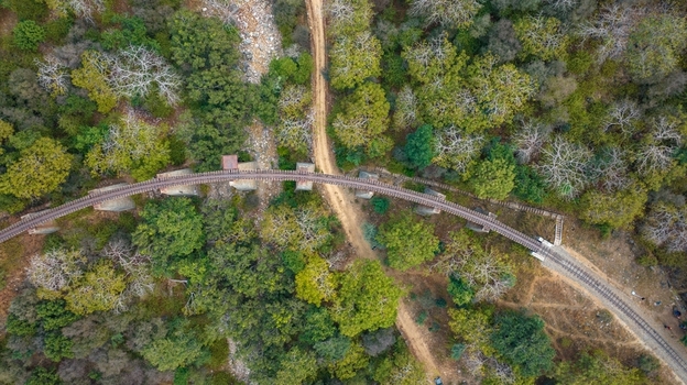Aerial view of a curved railway bridge crossing over a dry riverbed and a dirt path surrounded by dense green forest in Jodhpur Rajasthan India. Aerial view of a curved railway bridge crossing over a dry riverbed and a dirt path surrounded by dense green forest in Jodhpur Rajasthan India.
