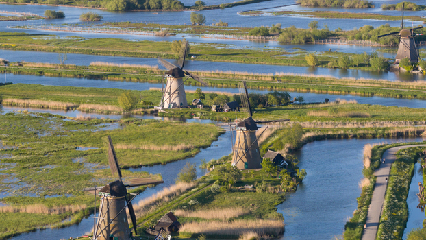 Aerial view of historic windmills standing along winding canals and lush green wetlands under bright sunlight Kinderdijk South Holland Netherlands. Aerial view of historic windmills standing along winding canals and lush green wetlands under bright sunlight Kinderdijk South Holland Netherlands.