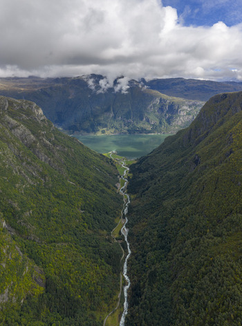 Aerial view of Sandvinvatnet lake and a winding river flowing through a deep valley between steep mountain slopes under low clouds Ullensvang Vestland Norway.