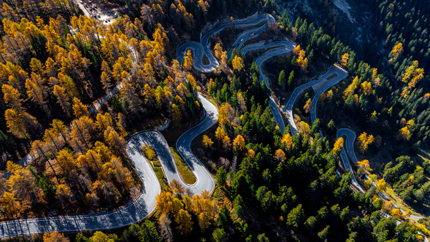 Aerial view of the winding Maloja Pass road surrounded by vibrant autumn larch trees and evergreen forests in the mountains of Bregaglia Grisons Switzerland. Aerial view of the winding Maloja Pass road surrounded by vibrant autumn larch trees and evergreen forests in the mountains of Bregaglia Grisons Switzerland.