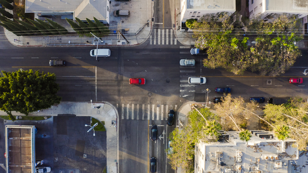 Aerial view of a busy city intersection with cars driving on asphalt roads crosswalks and surrounding trees in Los Angeles California United States.