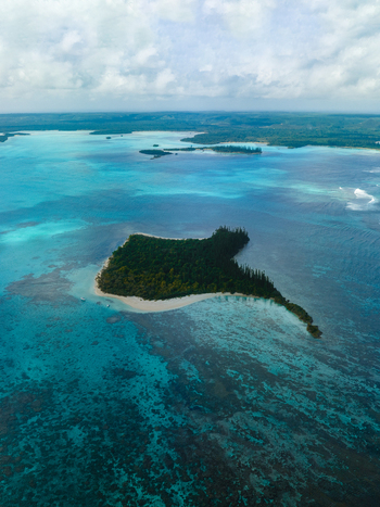 Aerial view of an island covered in dense green trees surrounded by turquoise waters the reef patterns visible beneath the surface Noumea New Caledonia. Aerial view of an island covered in dense green trees surrounded by turquoise waters the reef patterns visible beneath the surface Noumea New Caledonia.