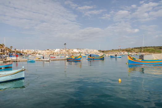 View of vibrant colorful fishing boats bob gently on the tranquil deep blue water under a soft cloudy sky Marsaxlokk Malta. View of vibrant colorful fishing boats bob gently on the tranquil deep blue water under a soft cloudy sky Marsaxlokk Malta.