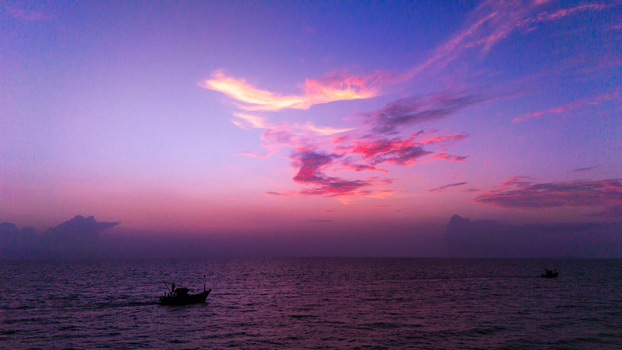 Aerial view of fishing boats sailing on the calm sea under a purple and pink sunset sky in South Goa Goa India.