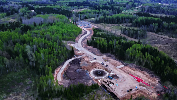 Aerial view of a wind turbine foundation under construction in a clearing surrounded by dense forest with a dirt access road leading to a nearby electrical substation in Latvija. Aerial view of a wind turbine foundation under construction in a clearing surrounded by dense forest with a dirt access road leading to a nearby electrical substation in Latvija.