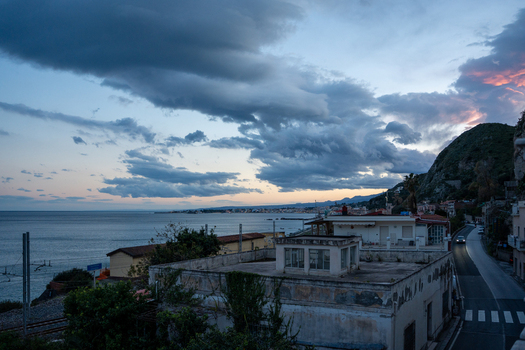 View of a dramatic coastal scene unfolds with the sea meeting the sky under a blanket of swirling clouds a road winds beside buildings Taormina Catania Italy. View of a dramatic coastal scene unfolds with the sea meeting the sky under a blanket of swirling clouds a road winds beside buildings Taormina Catania Italy.