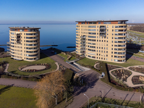 Aerial view of two modern buildings stand as sentinels against the tranquil blue waters their curved facades reflecting the clear sky Almere Netherlands. Aerial view of two modern buildings stand as sentinels against the tranquil blue waters their curved facades reflecting the clear sky Almere Netherlands.