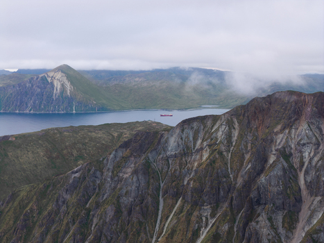 Aerial view of the rugged mountainous landscape of Unalaska Island with a cargo ship sailing in the bay under a cloudy sky in Unalaska Alaska United States.