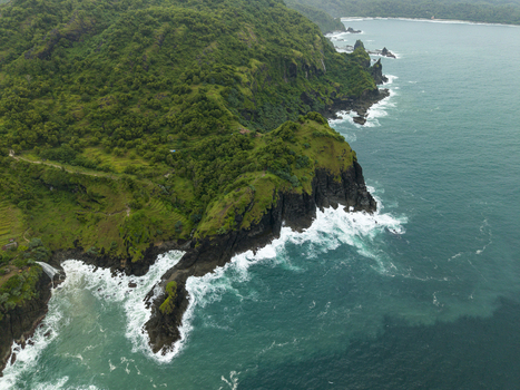 Aerial view of rugged cliffs cloaked in vibrant green vegetation meet the turquoise sea at Pengilon Hill Gunungkidul Regency Indonesia. Aerial view of rugged cliffs cloaked in vibrant green vegetation meet the turquoise sea at Pengilon Hill Gunungkidul Regency Indonesia.
