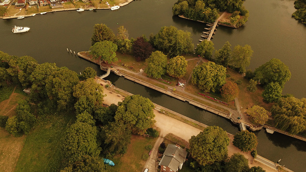 Aerial view of Thames River lock surrounded by lush green trees and parkland with a small boat navigating the waterway in Thames United Kingdom. Aerial view of Thames River lock surrounded by lush green trees and parkland with a small boat navigating the waterway in Thames United Kingdom.