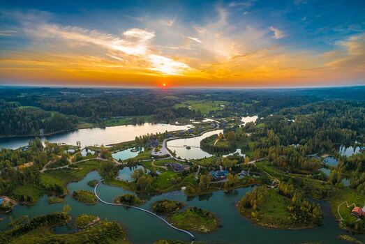 Aerial view of Amatciems village with wooden houses interconnected lakes lush forests and winding paths under a golden hour sunset sky in Amatciems Cesu novads Latvia. Aerial view of Amatciems village with wooden houses interconnected lakes lush forests and winding paths under a golden hour sunset sky in Amatciems Cesu novads Latvia.