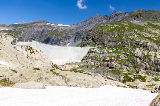 View of the VerticAlp Emosson dam set against rugged mountain peaks with rocky slopes patches of snow and lush green vegetation in Le Chatelard Valais Switzerland. View of the VerticAlp Emosson dam set against rugged mountain peaks with rocky slopes patches of snow and lush green vegetation in Le Chatelard Valais Switzerland.