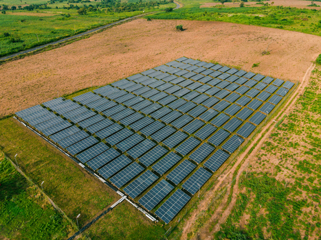 Aerial view of a solar farm with rows of photovoltaic panels installed in a rural landscape surrounded by green fields and dirt paths in Ogun State Nigeria.