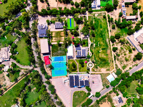 Aerial view of solar power panels installed on building rooftops surrounded by vibrant green lawns sports courts and lush trees in Dera Ghazi Khan Punjab Pakistan.