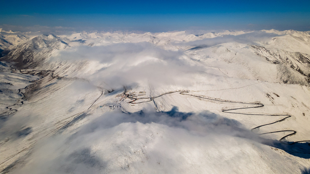 Aerial view of the winding mountain road at Babusar Pass surrounded by snow capped peaks and thick white clouds under a clear blue sky Babusar KPK Pakistan. Aerial view of the winding mountain road at Babusar Pass surrounded by snow capped peaks and thick white clouds under a clear blue sky Babusar KPK Pakistan.
