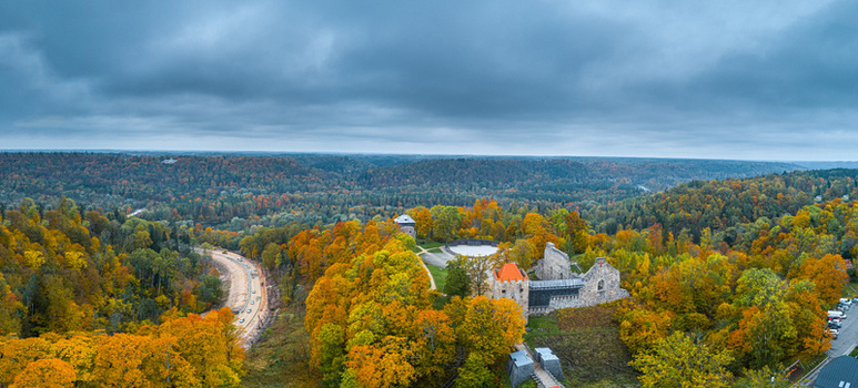 Aerial view of Sigulda Castle ruins surrounded by vibrant autumn forest winding road and cloudy sky in Sigulda Sigulda Municipality Latvia. Aerial view of Sigulda Castle ruins surrounded by vibrant autumn forest winding road and cloudy sky in Sigulda Sigulda Municipality Latvia.