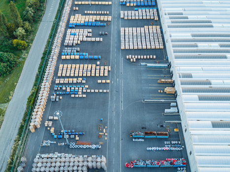 Aerial view of an industrial logistics yard featuring rows of wooden and blue cable reels a large warehouse building and paved storage areas in Italy. Aerial view of an industrial logistics yard featuring rows of wooden and blue cable reels a large warehouse building and paved storage areas in Italy.