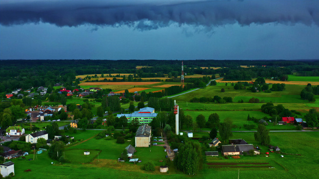 Aerial view of a rural landscape featuring green fields scattered houses and communication towers under a dramatic dark storm sky in Latvia. Aerial view of a rural landscape featuring green fields scattered houses and communication towers under a dramatic dark storm sky in Latvia.