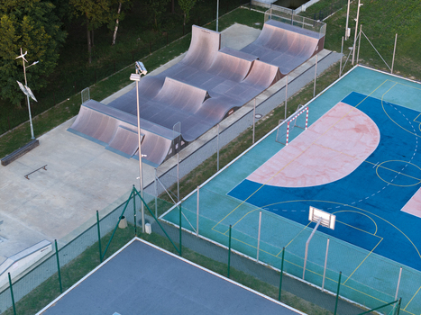 Aerial view of a skatepark with ramps and a multi sport court featuring blue and green surfaces in Poland.