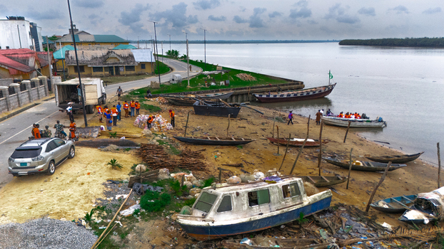Aerial view of a riverbank with wooden boats moored on the sandy shore a truck being loaded by workers and nearby buildings along the road in Minima Rivers Nigeria.
