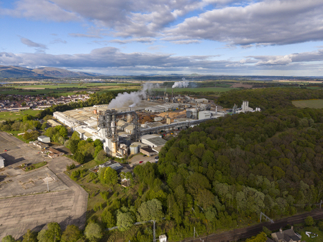 Aerial view of the industrial factory complex with smoke rising from chimneys surrounded by green forests and residential areas in Cowie Scotland United Kingdom. Aerial view of the industrial factory complex with smoke rising from chimneys surrounded by green forests and residential areas in Cowie Scotland United Kingdom.