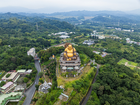 Aerial view of the giant golden Maitreya Buddha statue surrounded by lush green hills dense forest and winding roads in Jiuru Township Pingtung County Taiwan. Aerial view of the giant golden Maitreya Buddha statue surrounded by lush green hills dense forest and winding roads in Jiuru Township Pingtung County Taiwan.