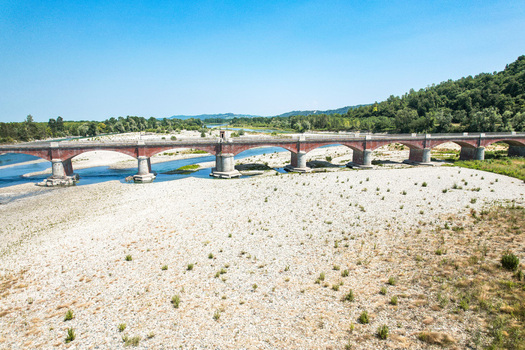 Aerial view of the historic brick arch bridge Ponte Crescentino spanning the dry riverbed of the Po River during a drought surrounded by green hills in Verrua Savoia Piemonte Italy. Aerial view of the historic brick arch bridge Ponte Crescentino spanning the dry riverbed of the Po River during a drought surrounded by green hills in Verrua Savoia Piemonte Italy.